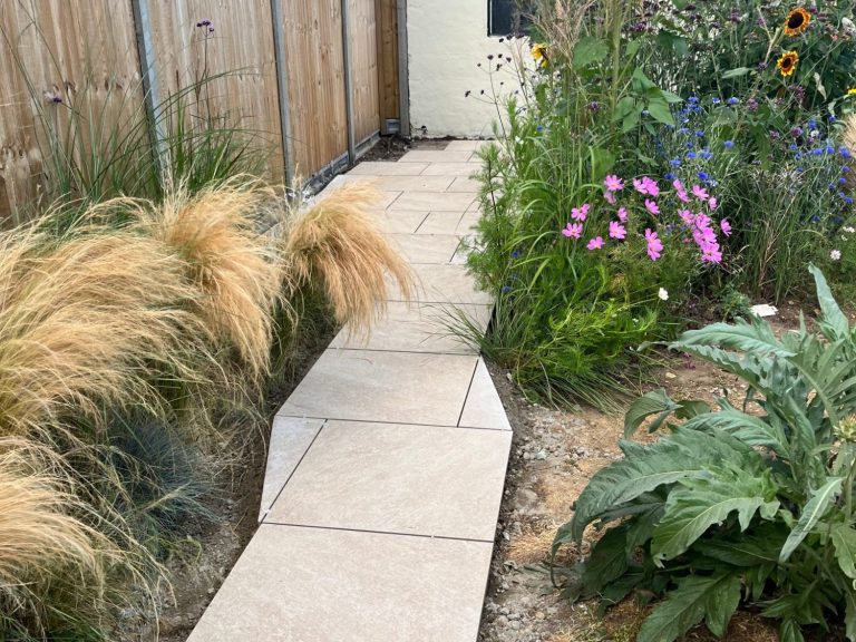 Paved garden pathway bordered by tall grasses and colourful flowers.